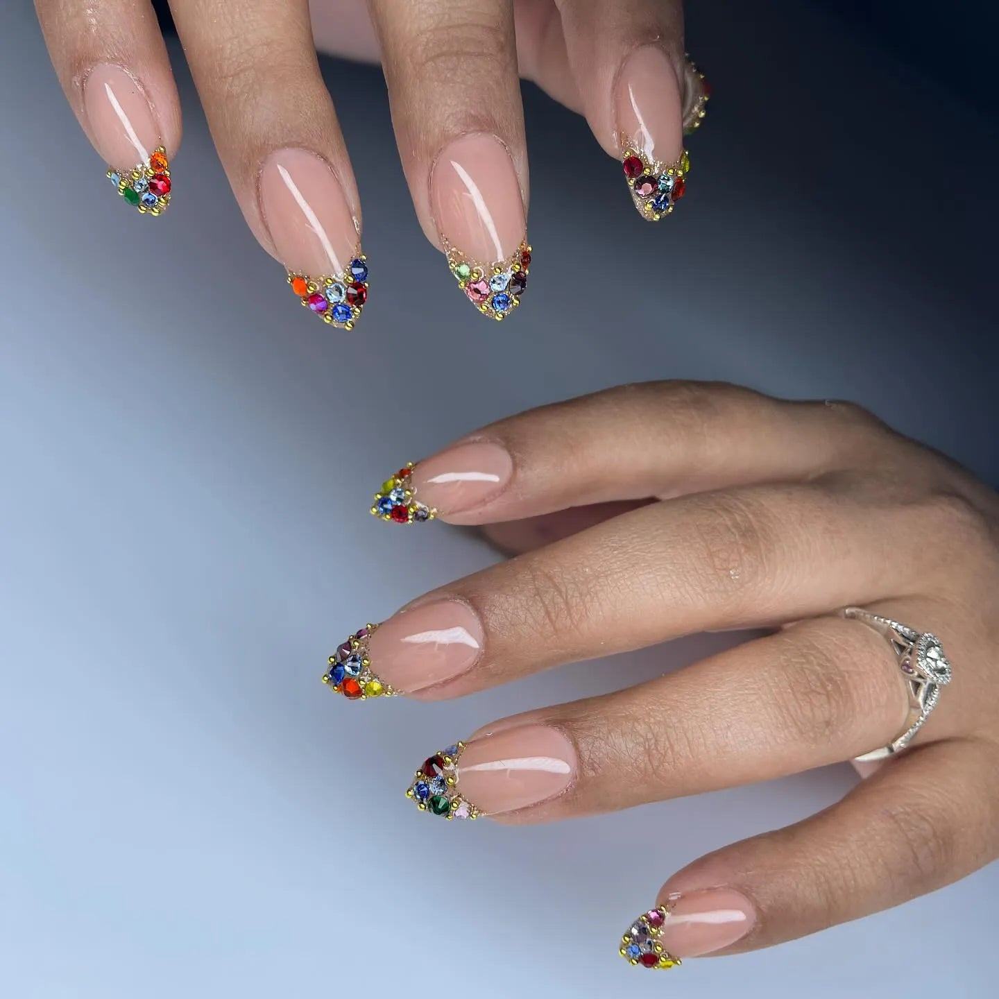Hand with nude press-on nails featuring rainbow crystal French tip design