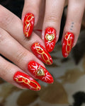 Handmade red press-on nails with golden chain designs, heart charms, and starburst accents.