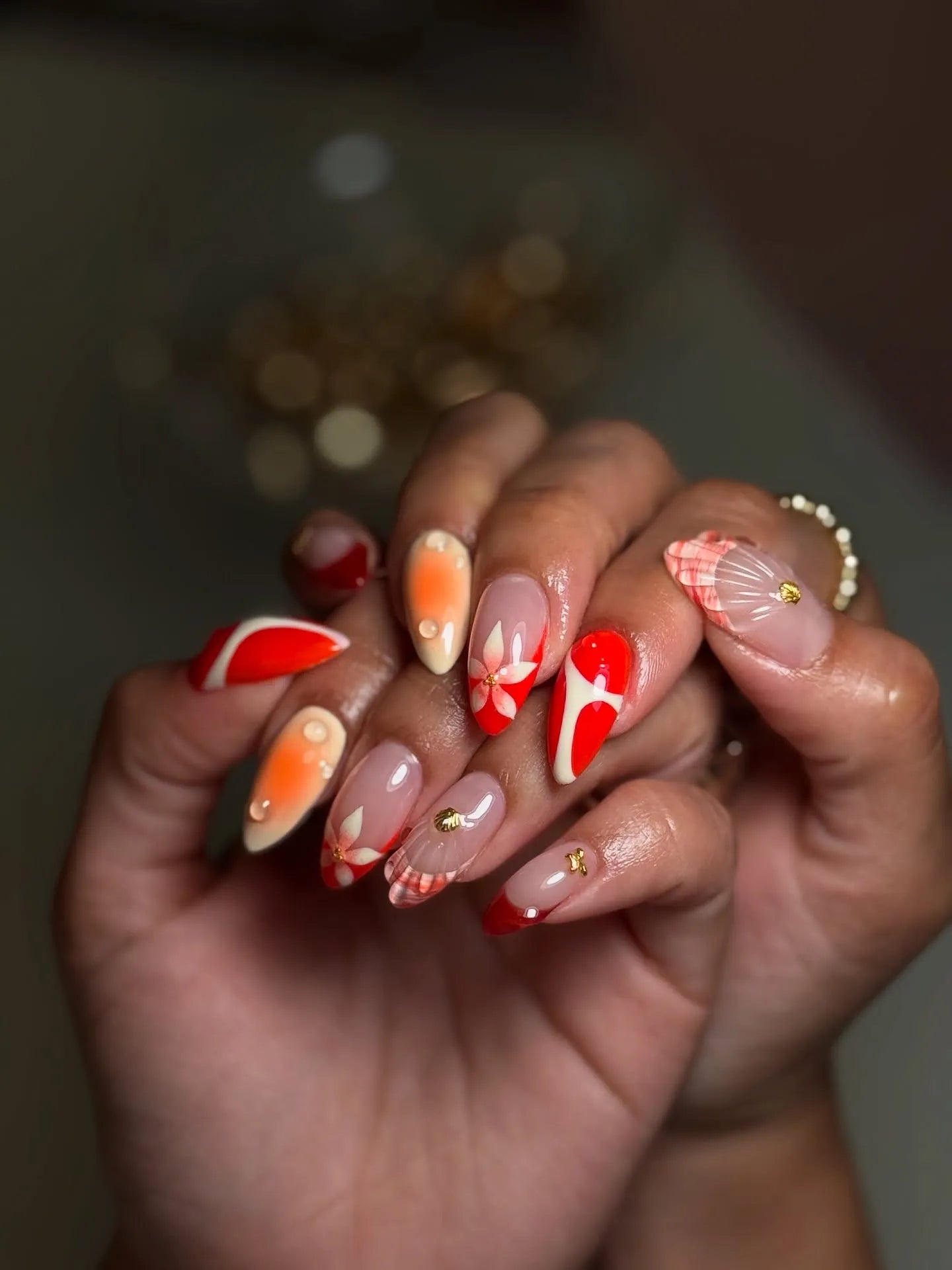 Hand with handmade red and tropical floral press-on nails featuring shell and aura designs.