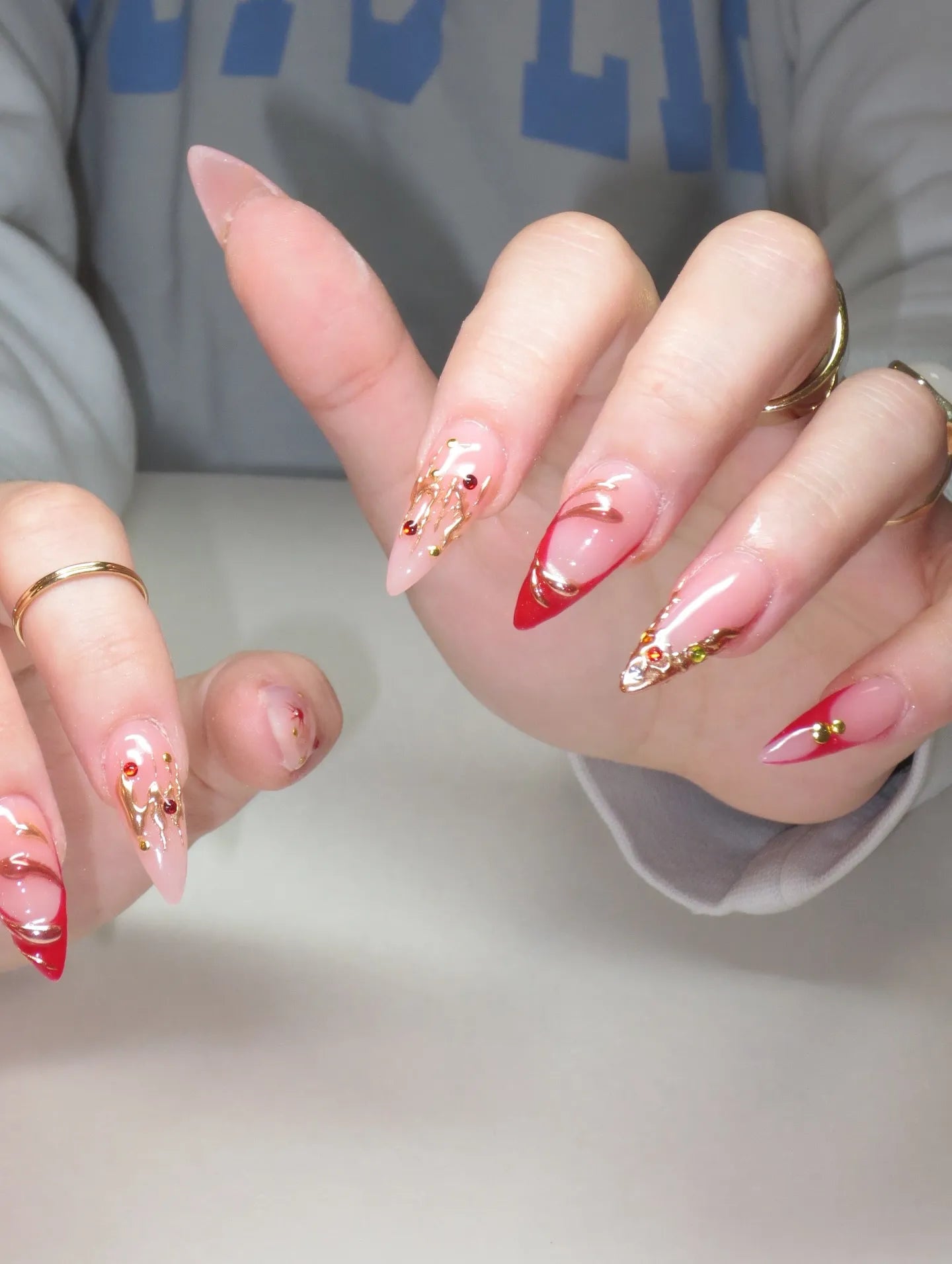 Hand with long press-on nails featuring red French tips and gold chrome festive designs