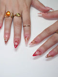 Hand with handmade press-on nails featuring red French tips, gold chrome drips, and festive accents.