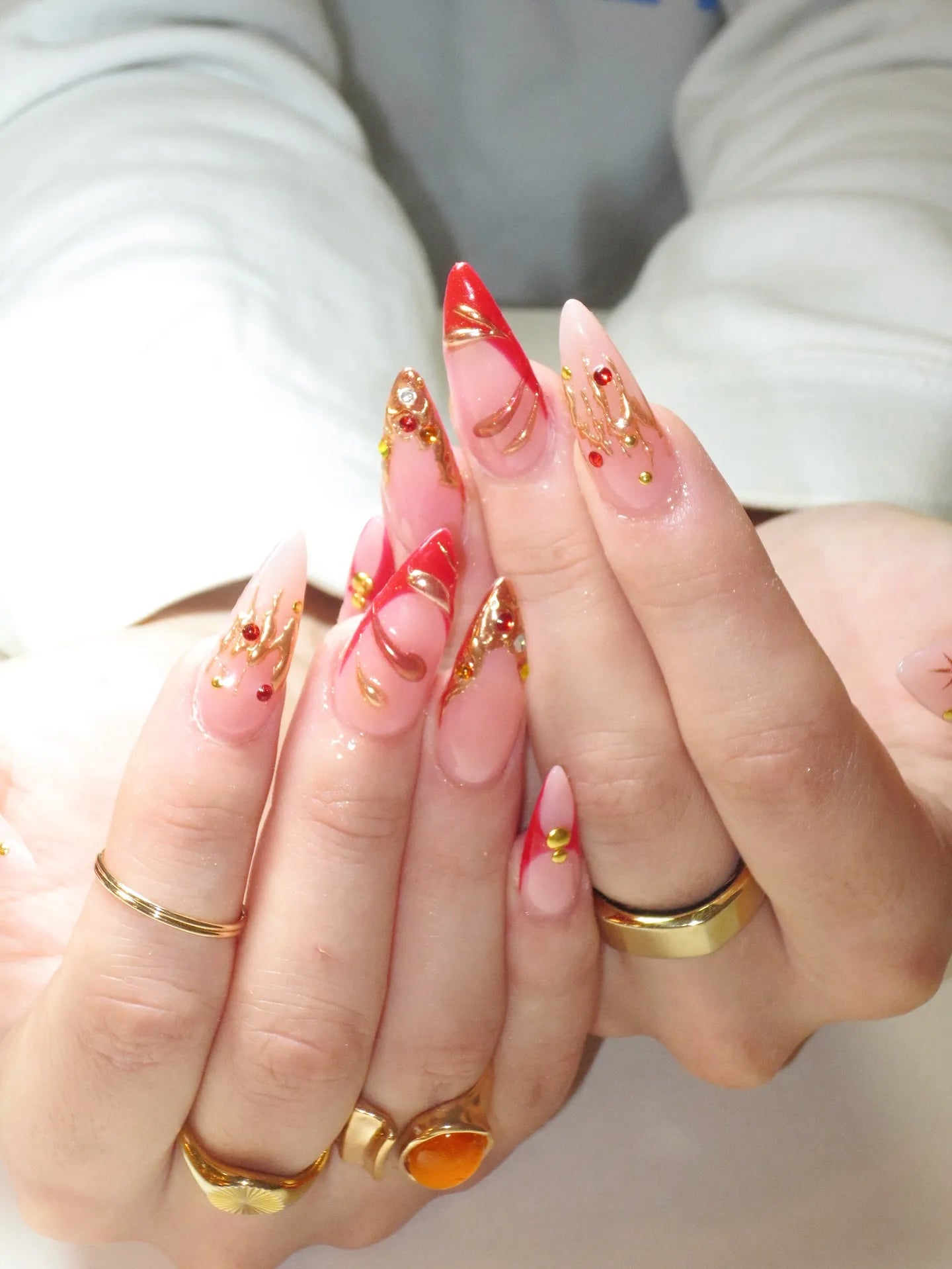 Hand holding handmade stiletto press-on nails with red French tips and gold chrome drip accents