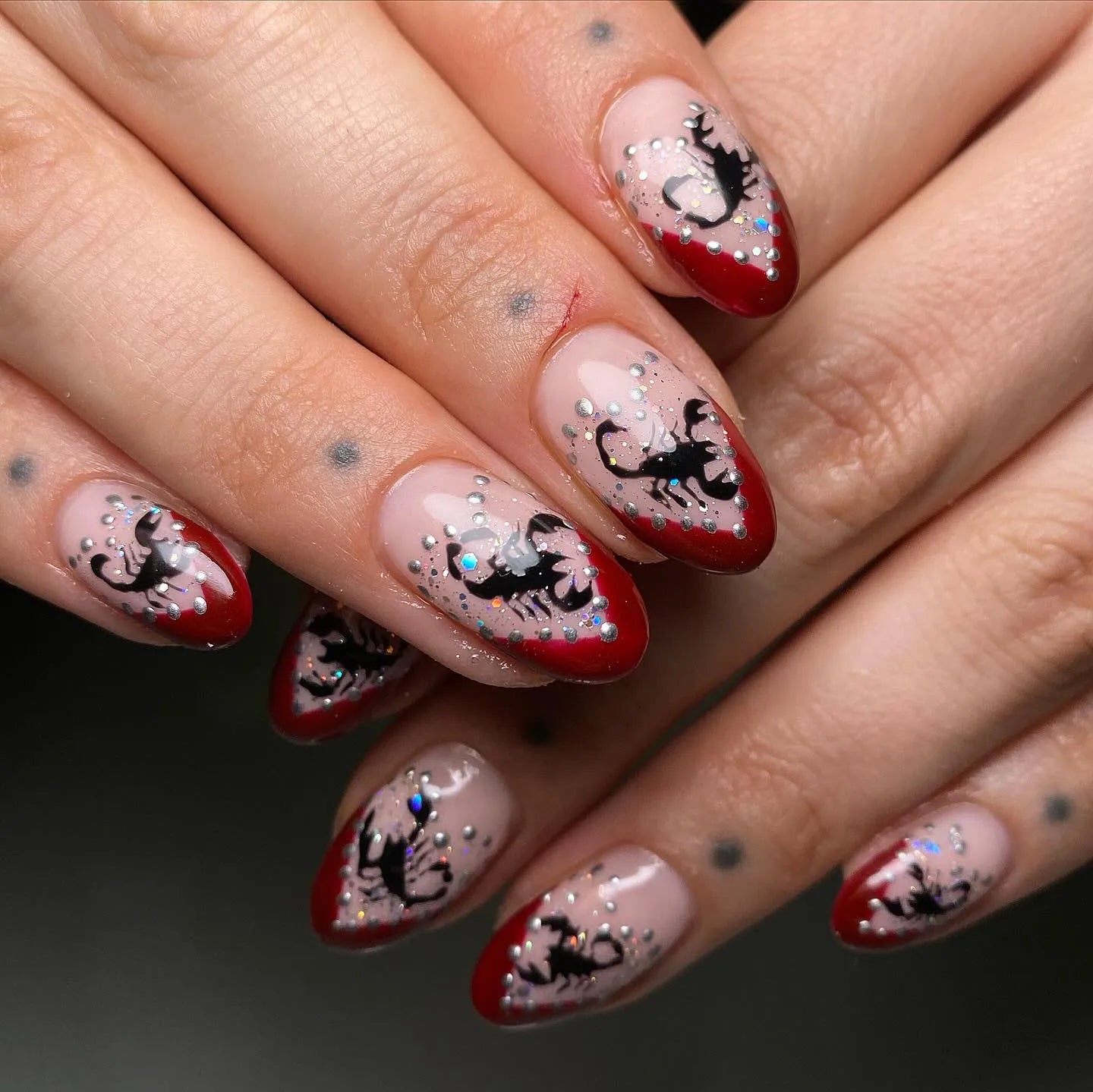Handmade press-on nails with red French tips, black scorpion art, and silver shimmer accents.