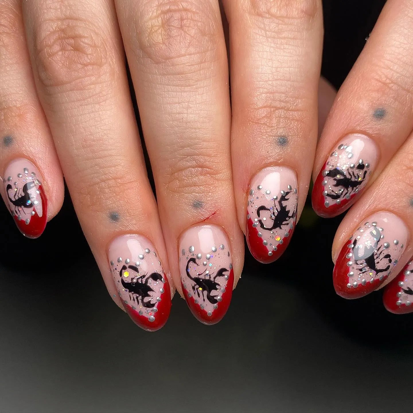 Handmade press-on nails with red French tips, black scorpion art, and silver glitter accents.