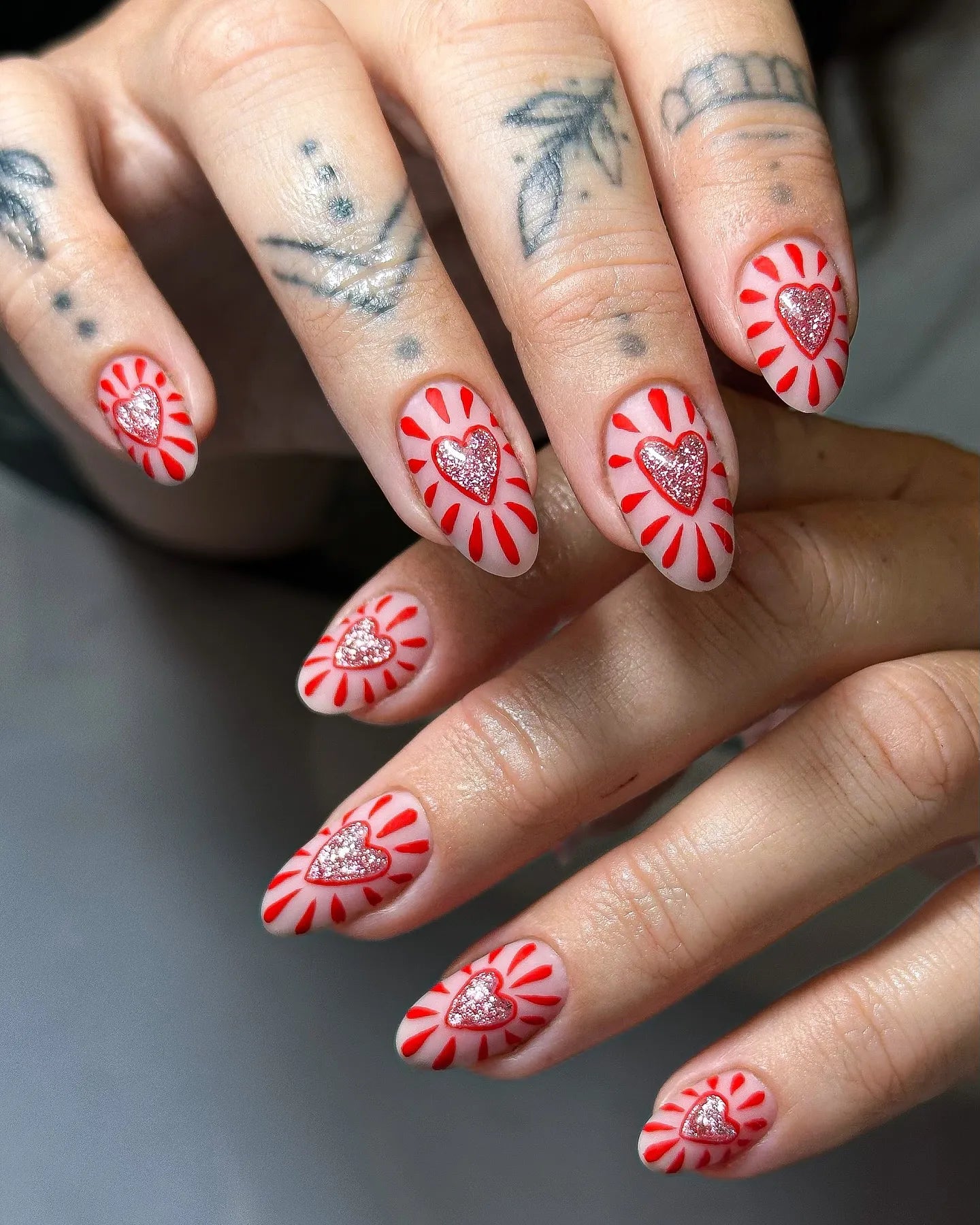 Handmade press-on nails with pink base, red sunburst design, and glitter heart accents