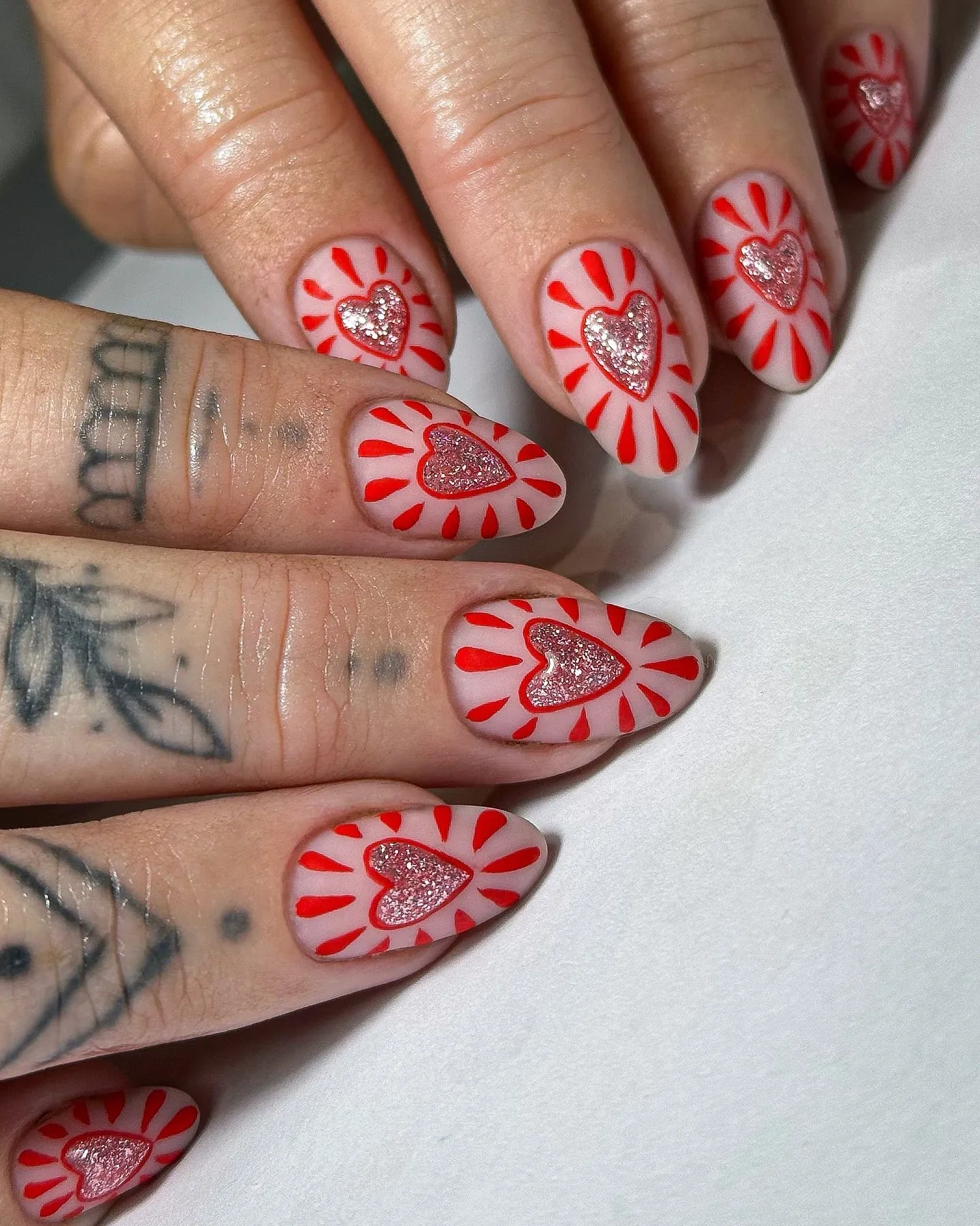 Handmade pink press-on nails with red sunburst design and glitter heart accents.
