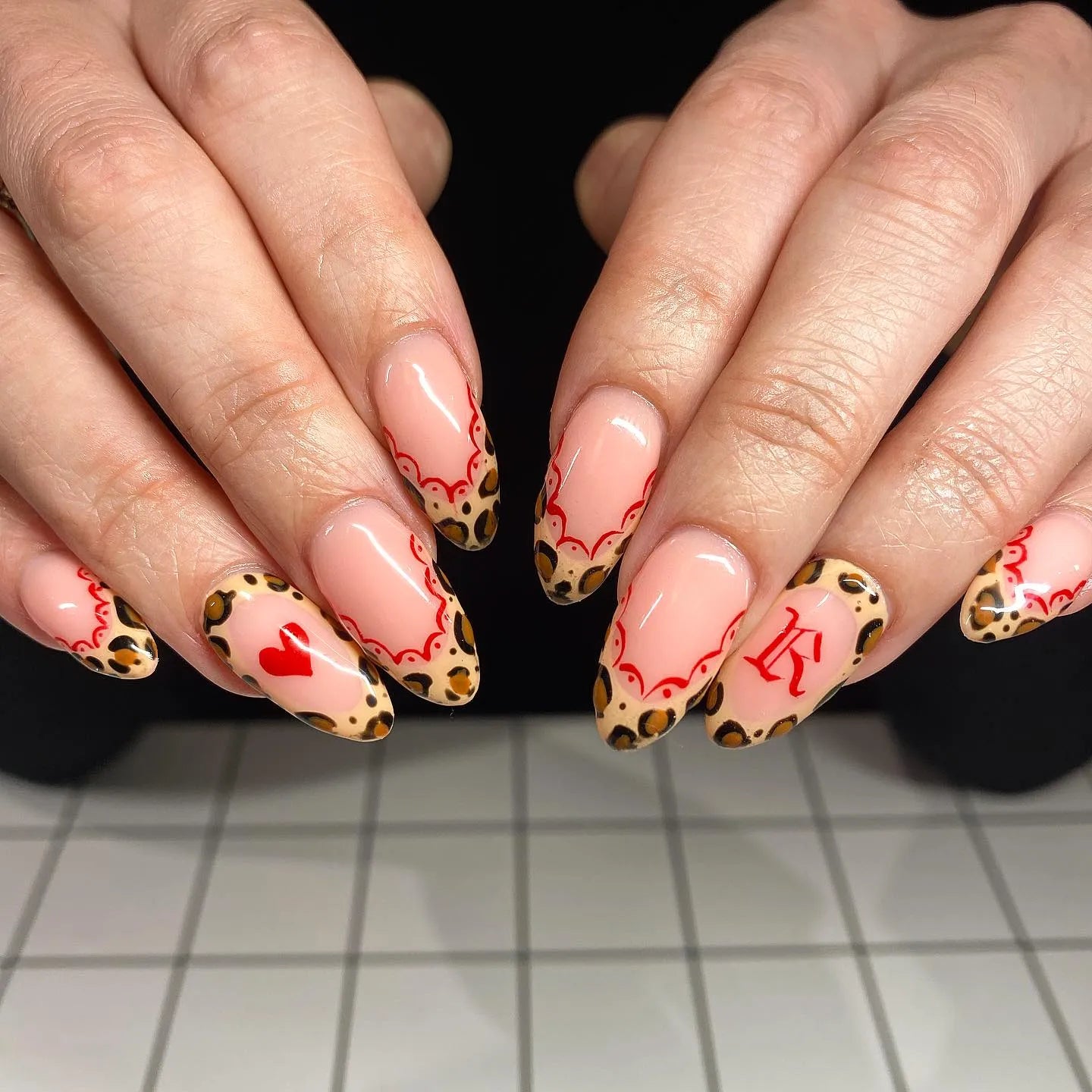 Hand with almond-shaped press-on nails, red lace French tips, leopard print and heart design.