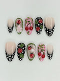 Handmade press-on nails with red ladybug, cherry, floral, and black polka dot designs.