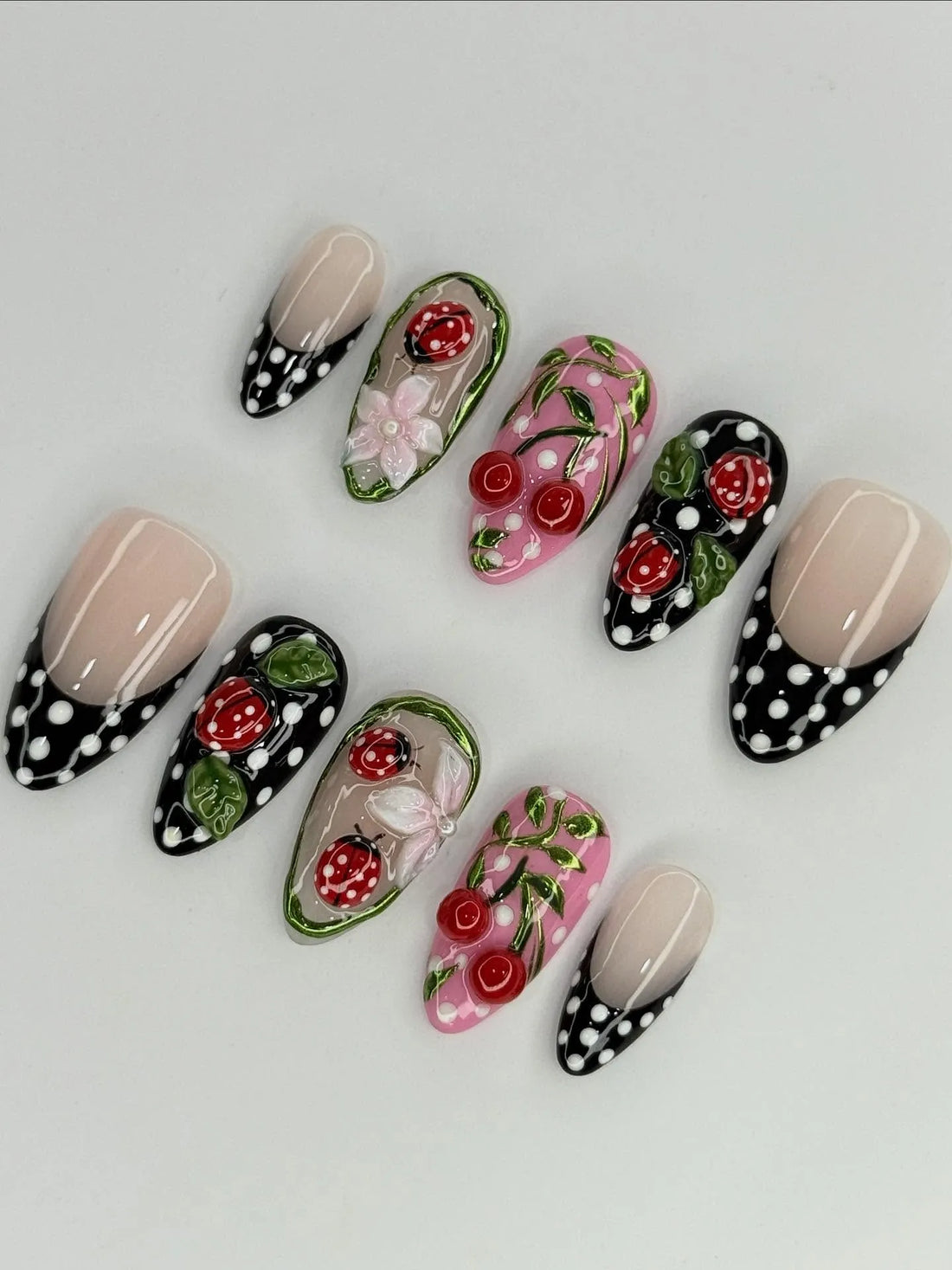 Handmade press-on nails with red ladybug, cherry, floral, and black polka dot designs.
