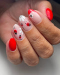 Hand with handmade press-on nails featuring red ladybugs, white flowers, and French tips.