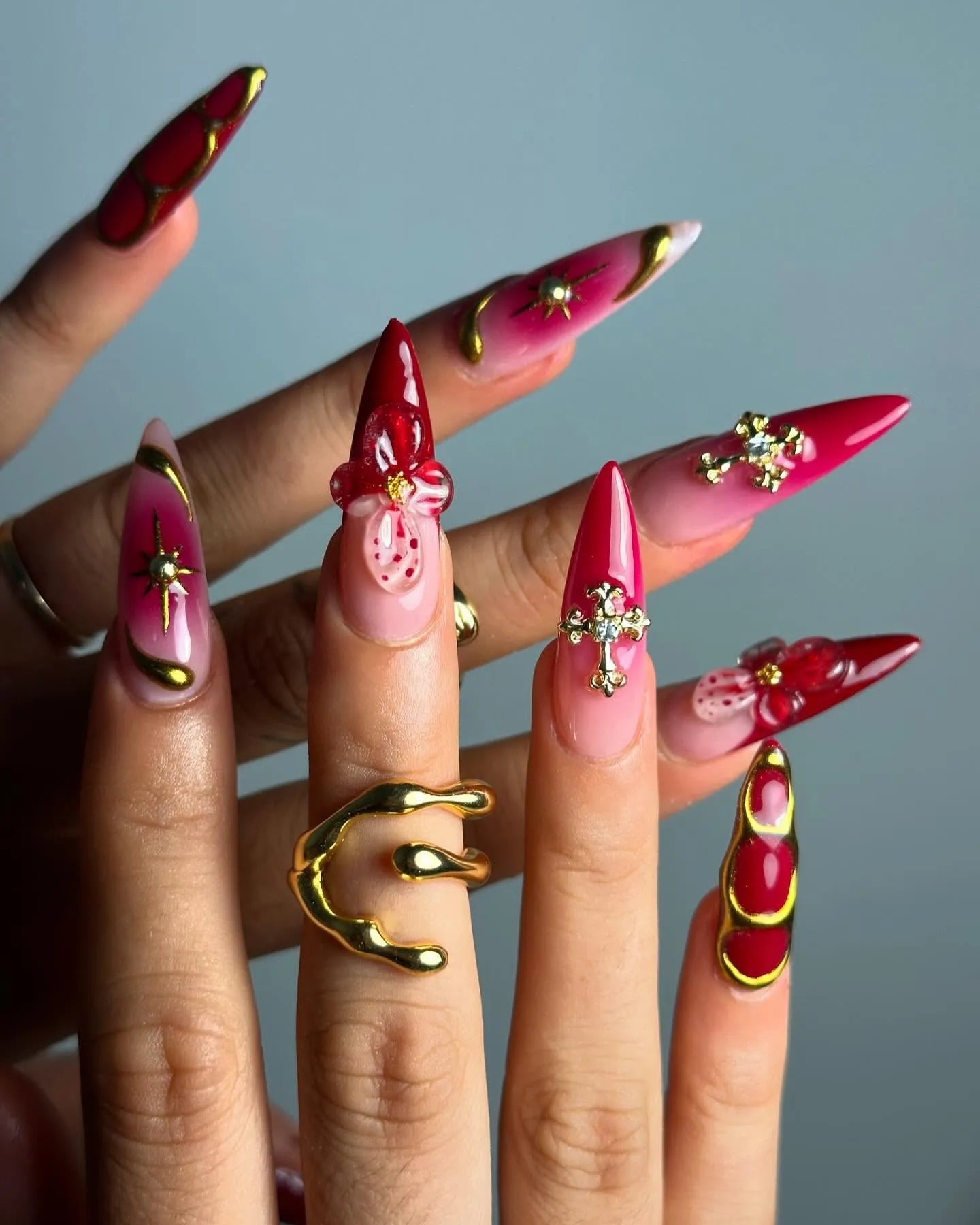 Handmade red and pink press-on nails with 3D floral, gold celestial, and cross art accents.