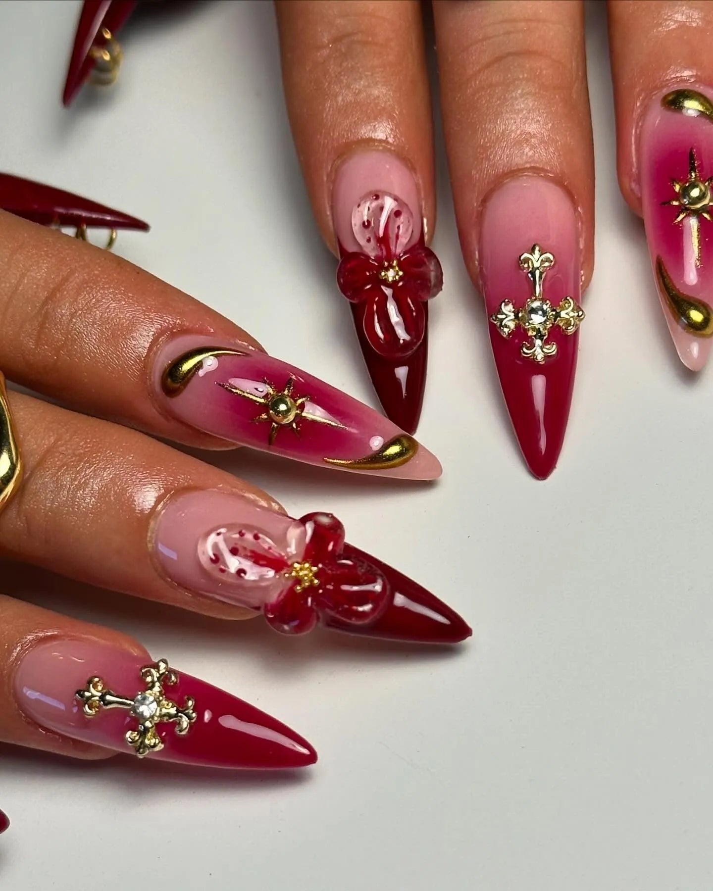 Handmade red and pink stiletto press-on nails with 3D floral, gold celestial, and cross art designs