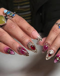 Handmade stiletto press-on nails with ruby red heart gems, gold filigree, and marble accents.