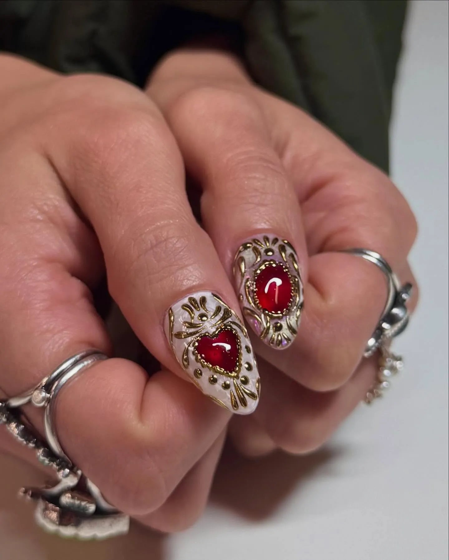 Hand with handmade stiletto press-on nails featuring ruby red heart gems and gold filigree.
