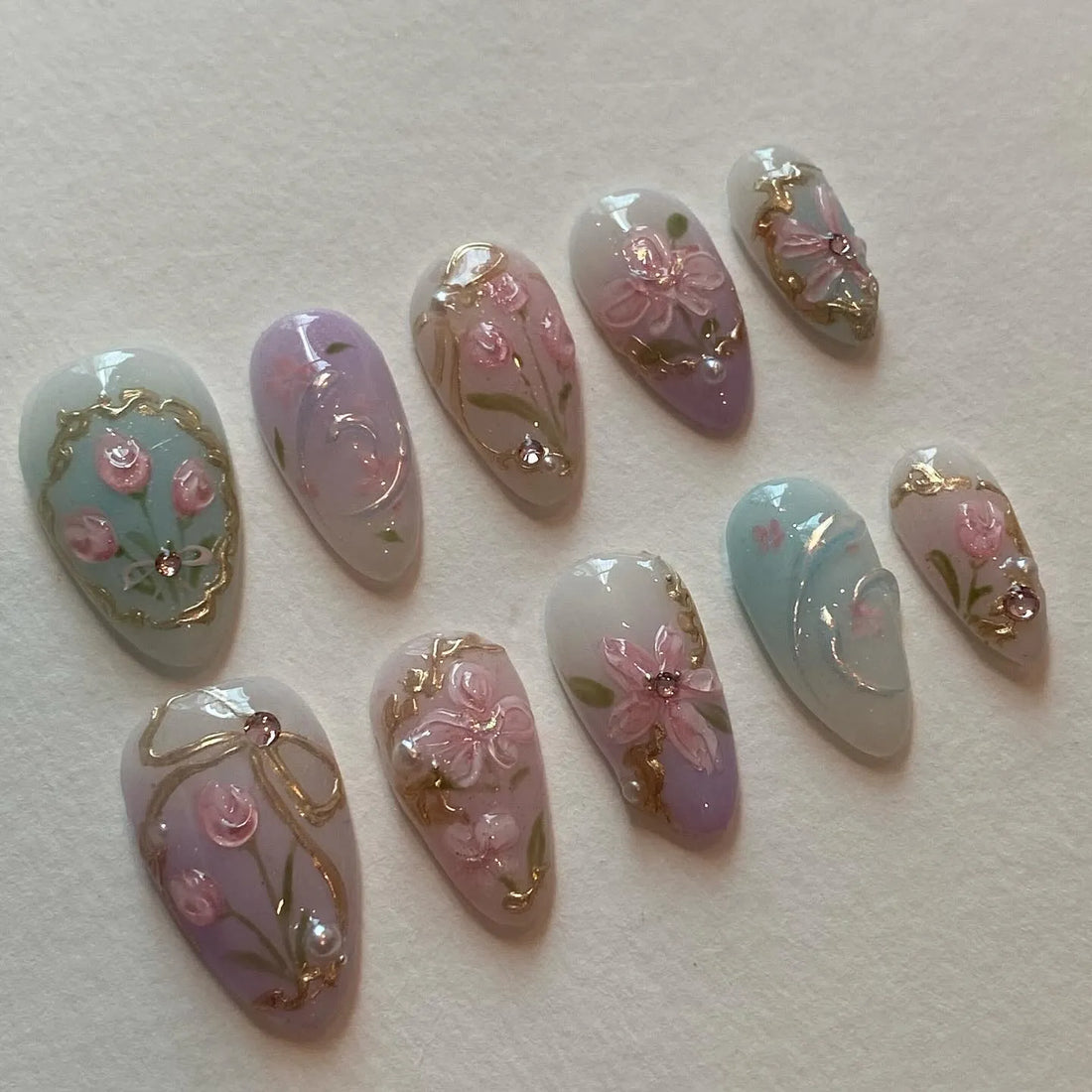 Handmade pastel press-on nails with pink floral designs, gold accents, and bow details.