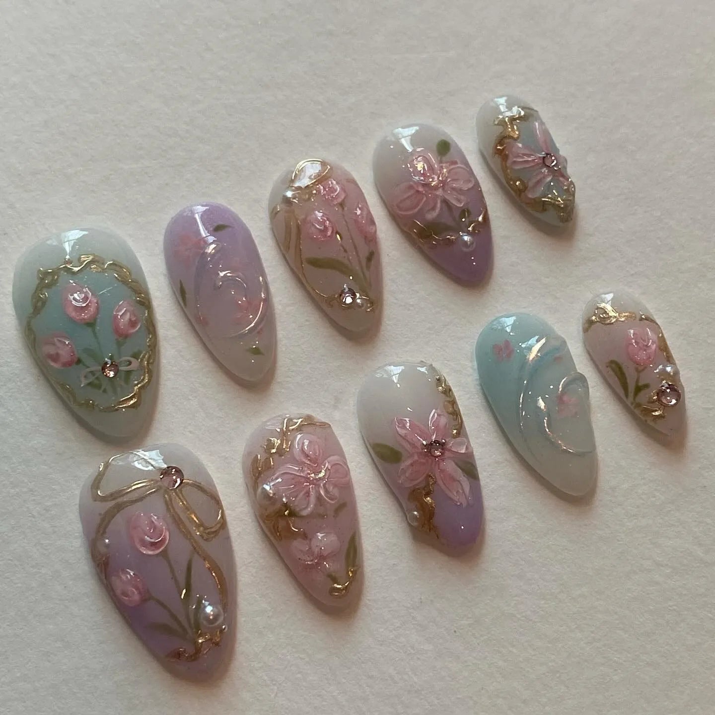 Handmade pastel pink and lilac floral press-on nails with gold frame and bow accents