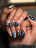 Hand with royal blue shimmer press-on nails featuring 3D pearl charms and starburst designs.