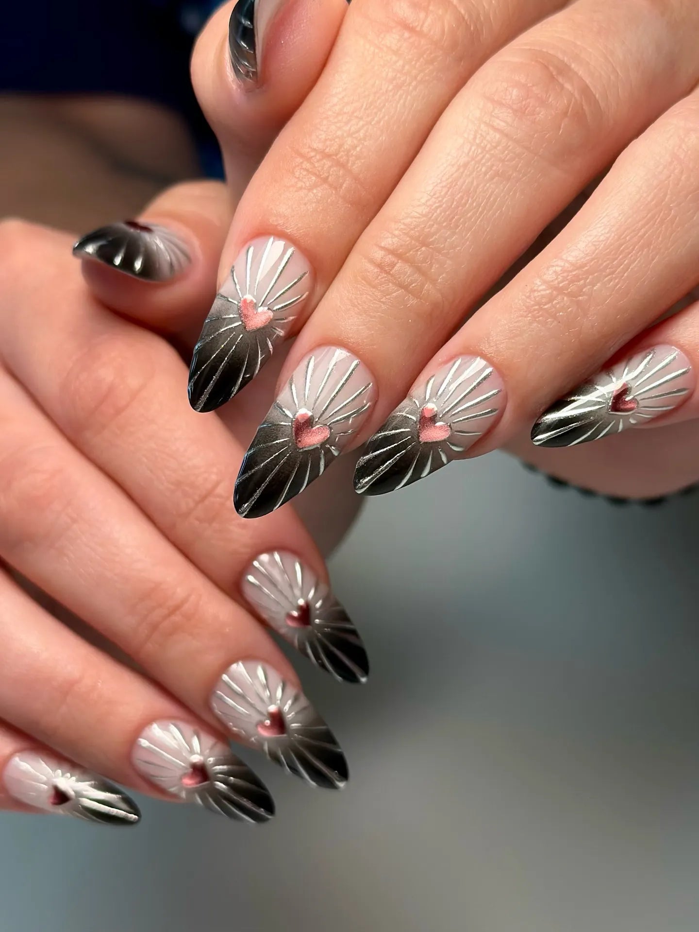 Hand with handmade chrome press-on nails featuring pink heart and sunburst 3D design.