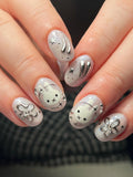 Hand with oval, shimmering silver press-on nails featuring celestial stars, bunny, and chrome ribbon designs.