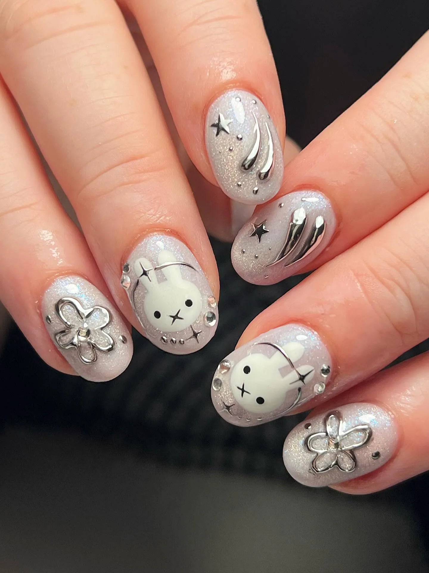 Hand with shimmering silver press-on nails featuring bunny, stars, and flower 3D designs