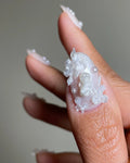 Hand holding iridescent press-on nail with 3D floral and pearl designs