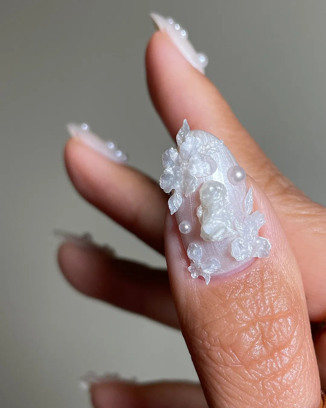 Hand holding iridescent press-on nail with 3D floral and pearl designs