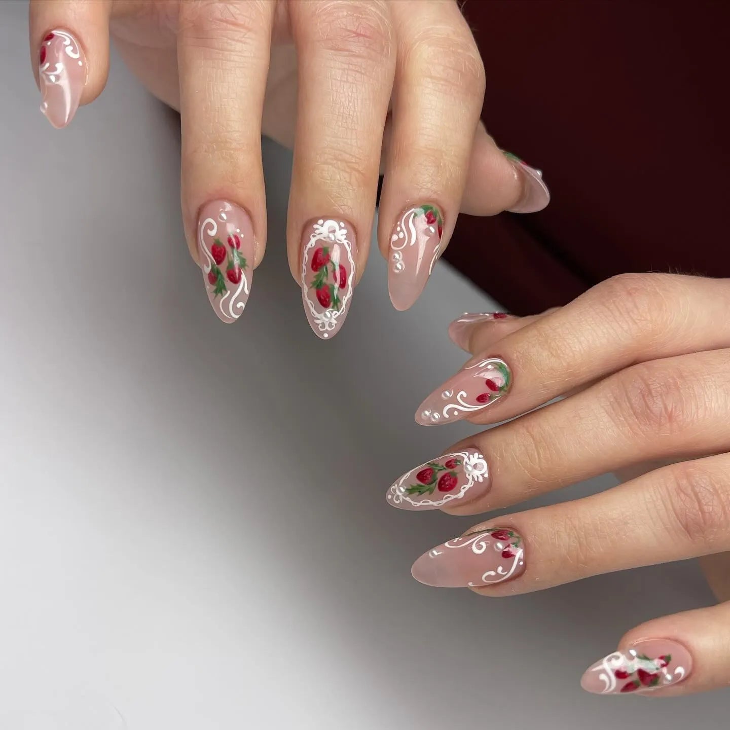 Hand with almond-shaped press-on nails featuring pink base, strawberry art, and white lace details.