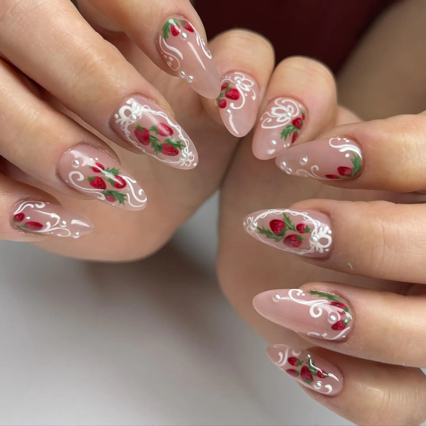 Handmade press-on nails with strawberry art, lace details, and pearl accents on almond tips
