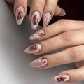 Hand with almond-shaped press-on nails featuring strawberry art, white lace tips, and pearl details.