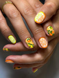 Hand with handmade press-on nails featuring citrus fruit designs in bright summer colors
