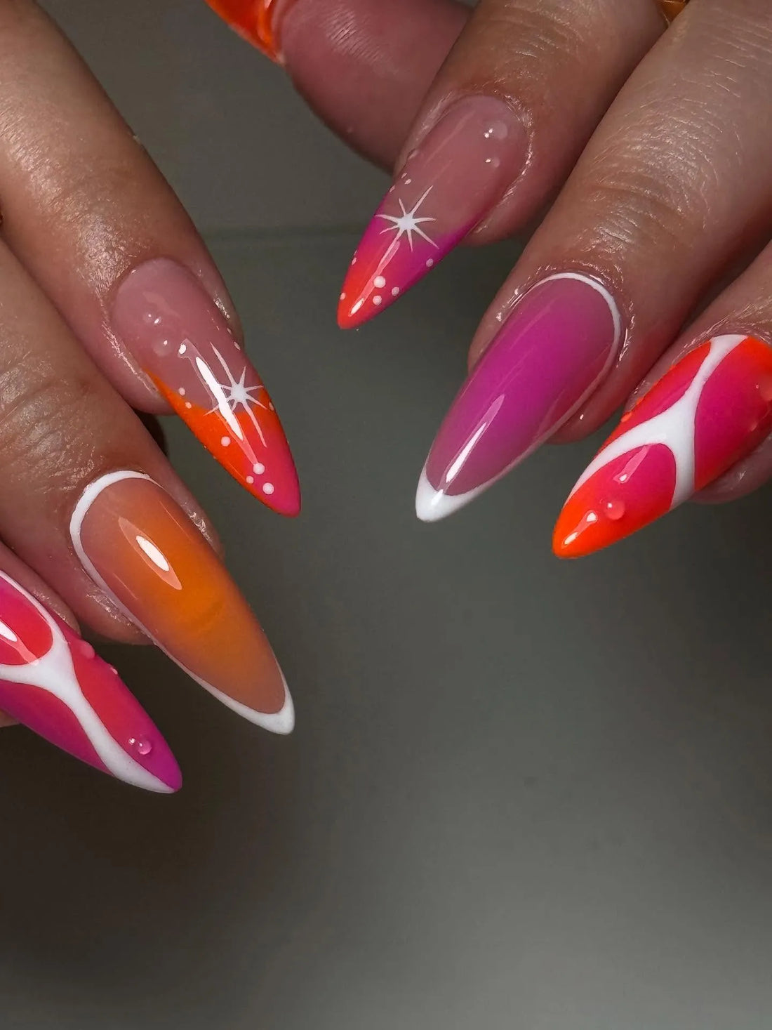Hand with long press-on nails in pink, orange, and white sunset aura gradient with abstract stars.