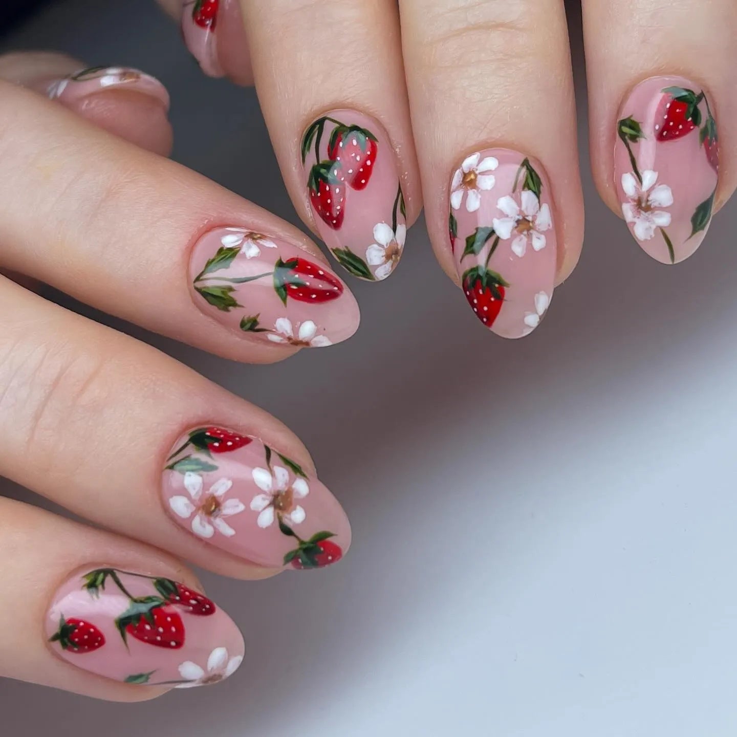 Handmade press-on nails with pink base, red strawberry and white floral design.