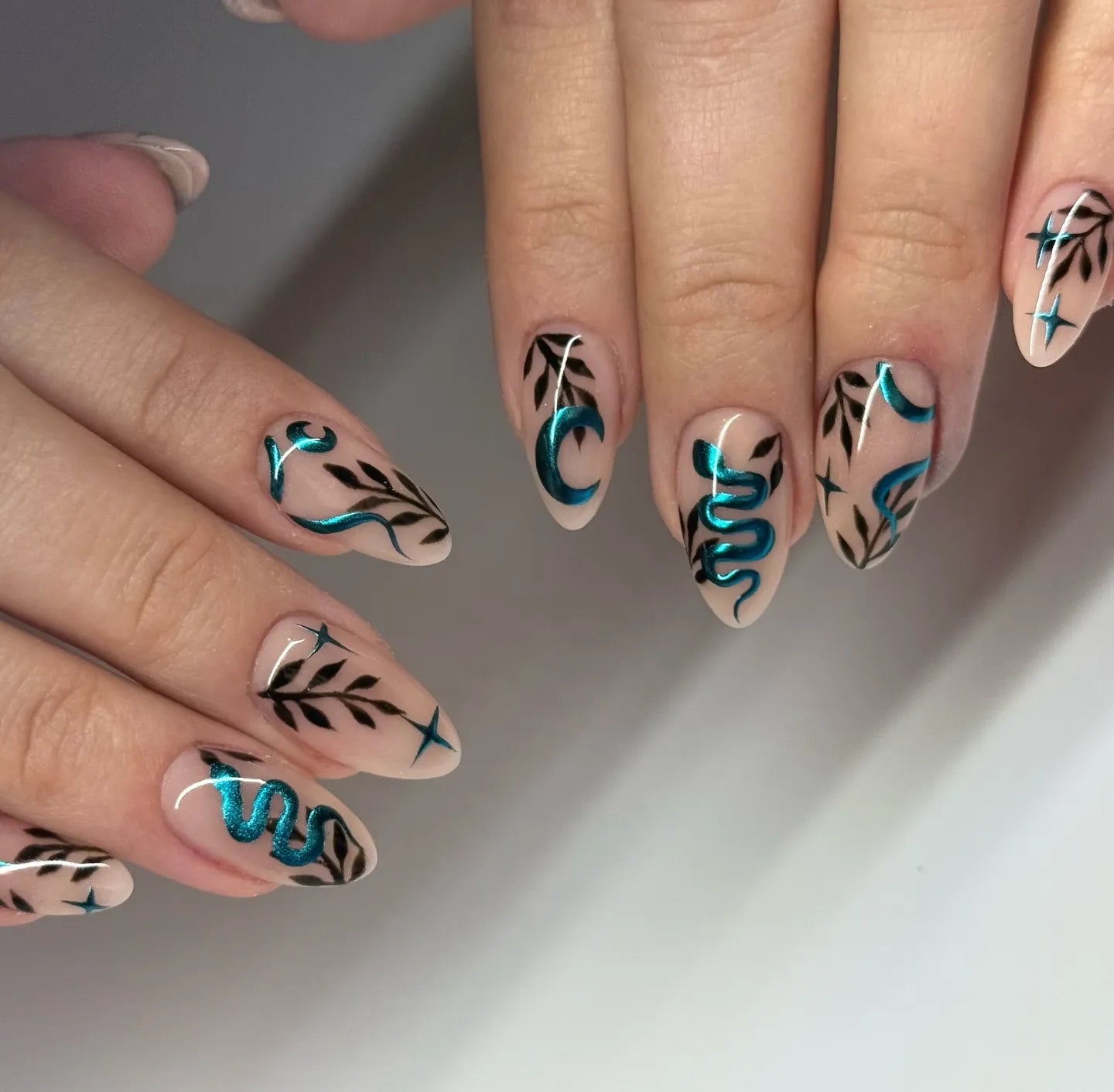 Handmade press-on nails with teal chrome snake, moon, and celestial designs on almond-shaped tips.