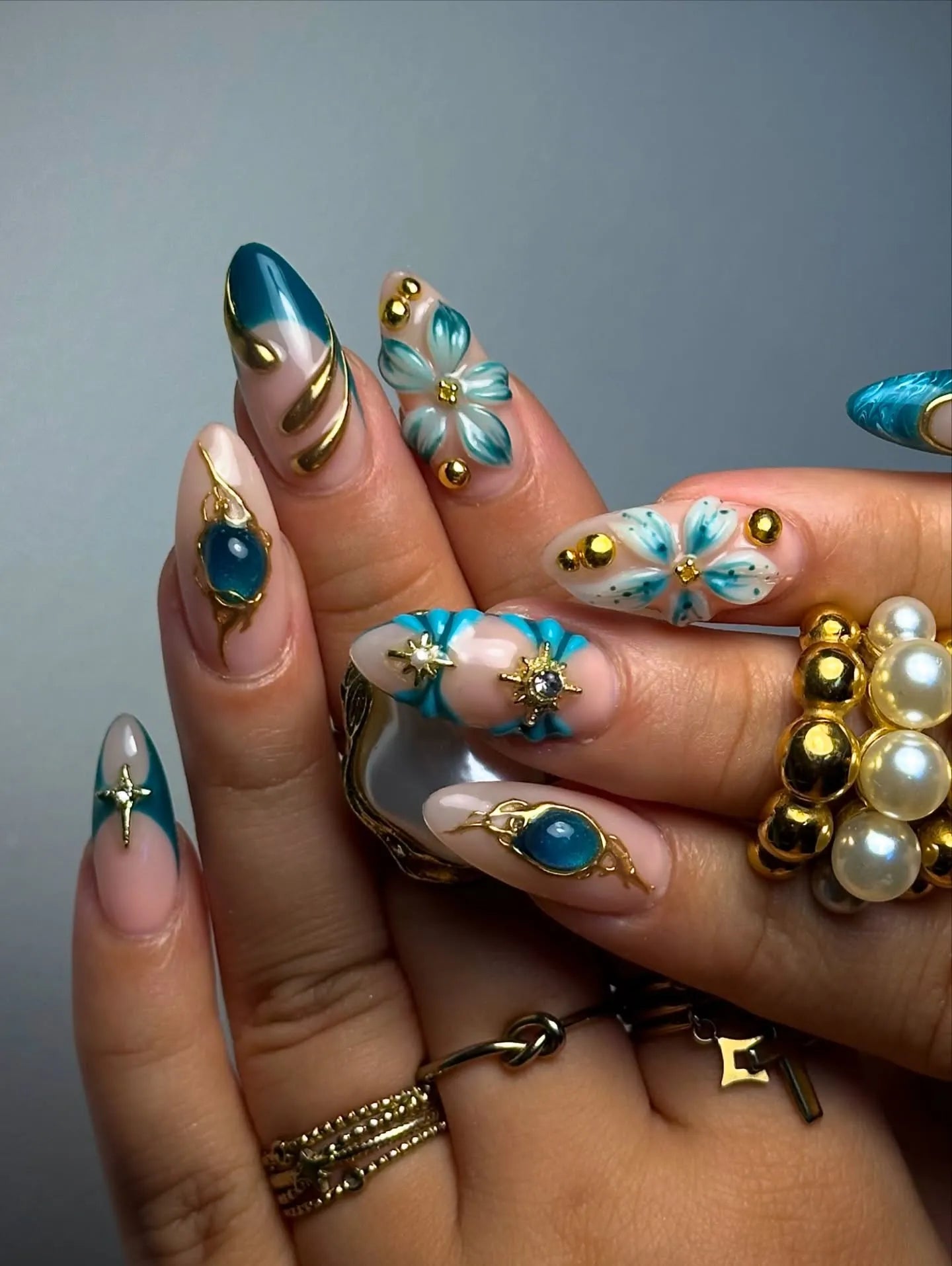 Hand with teal and gold celestial 3D floral press-on nails and jeweled accents