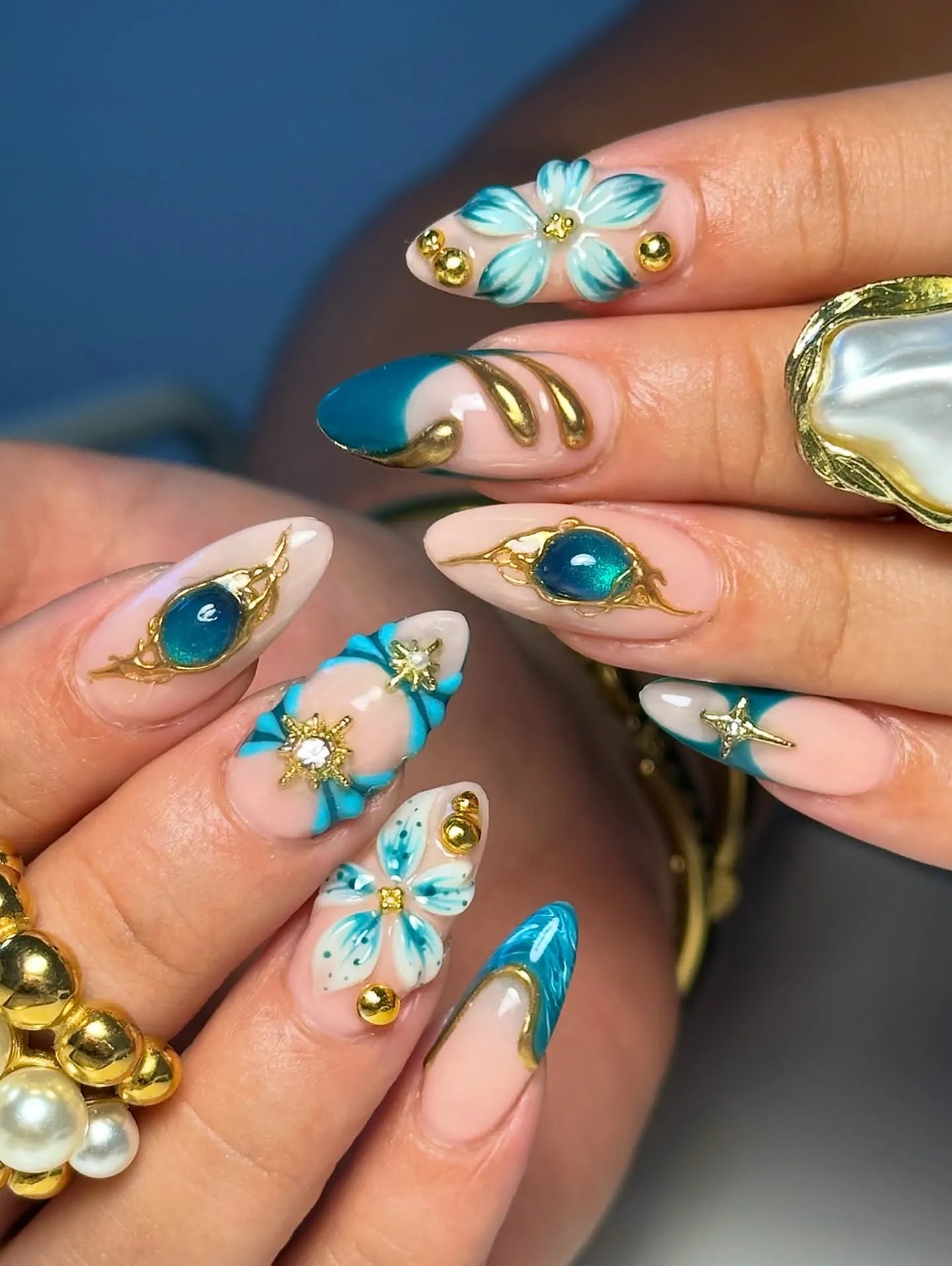 Handmade teal and gold press-on nails with 3D floral and celestial designs, luxury accents.