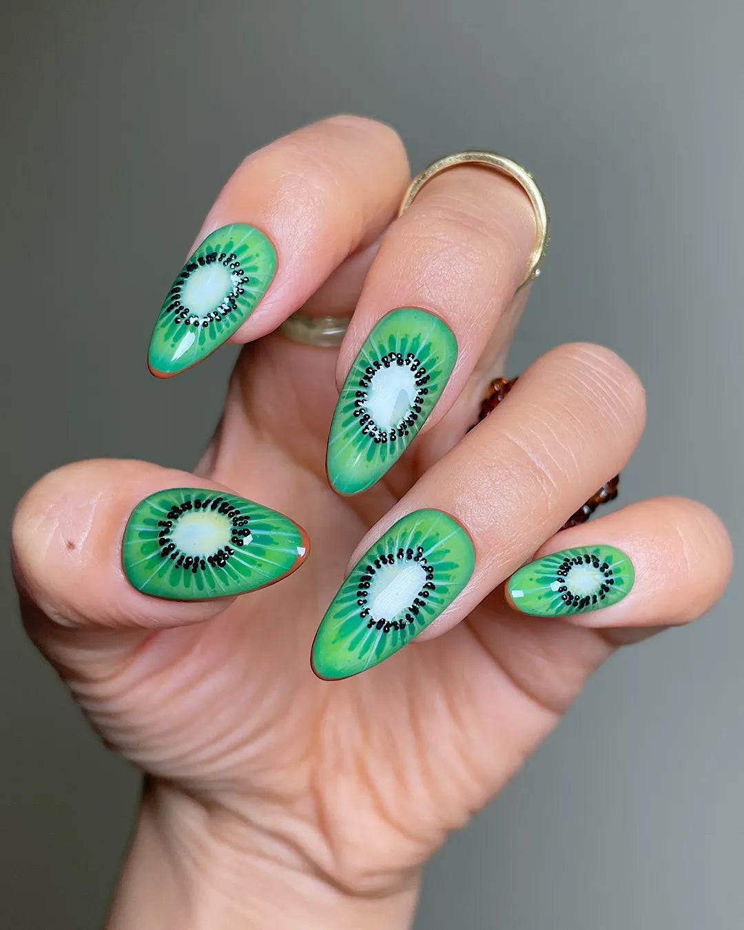 Hand with almond-shaped, green kiwi fruit themed handmade press-on summer nails