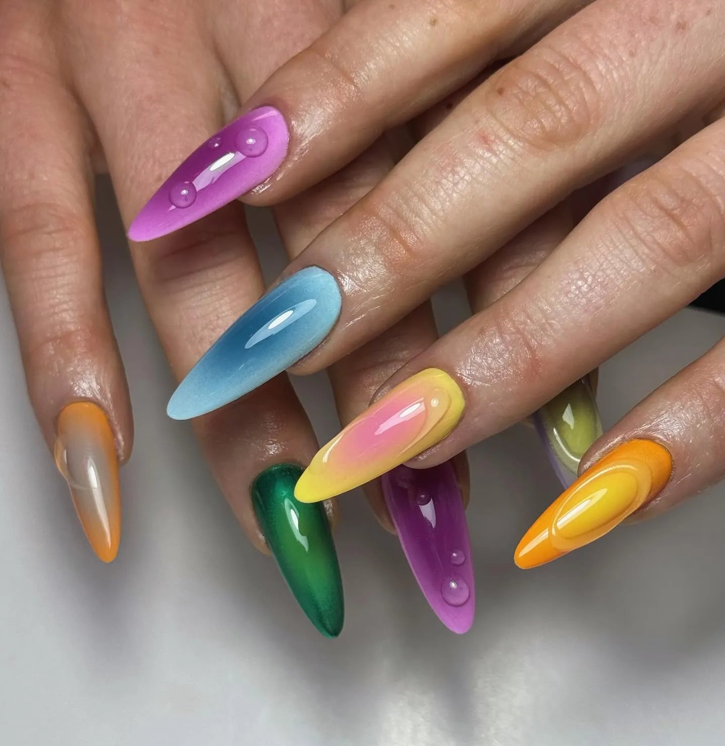 Hand with handmade vibrant rainbow chrome liquid drip press-on nails, glossy finish
