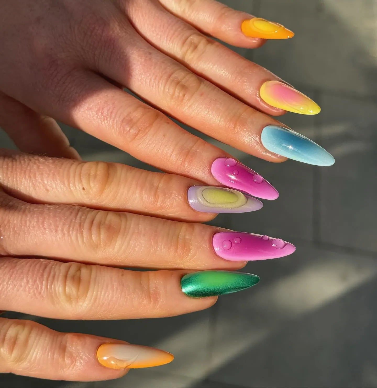 Hand with long press-on nails in vibrant rainbow chrome and liquid drip designs