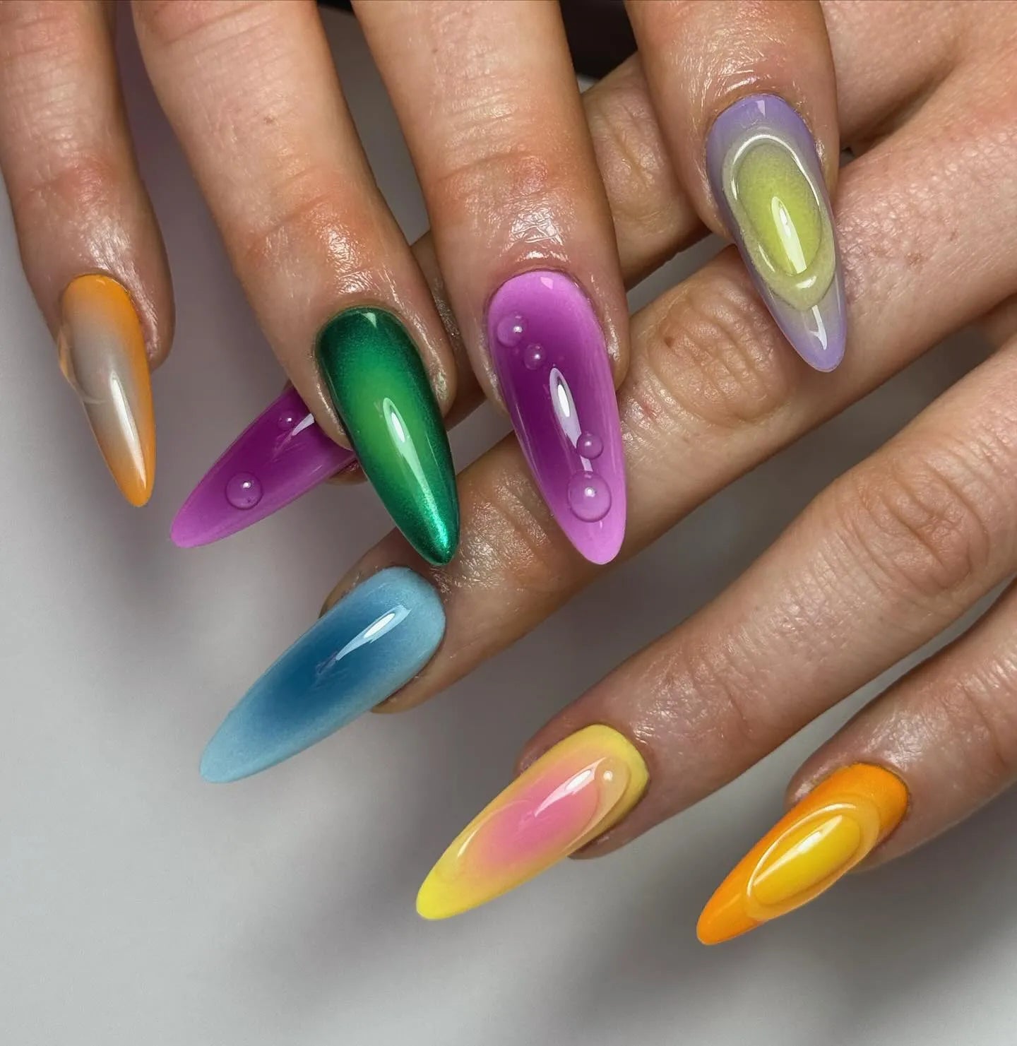 Hand with pointed, handmade press-on nails in vibrant rainbow chrome and drip designs