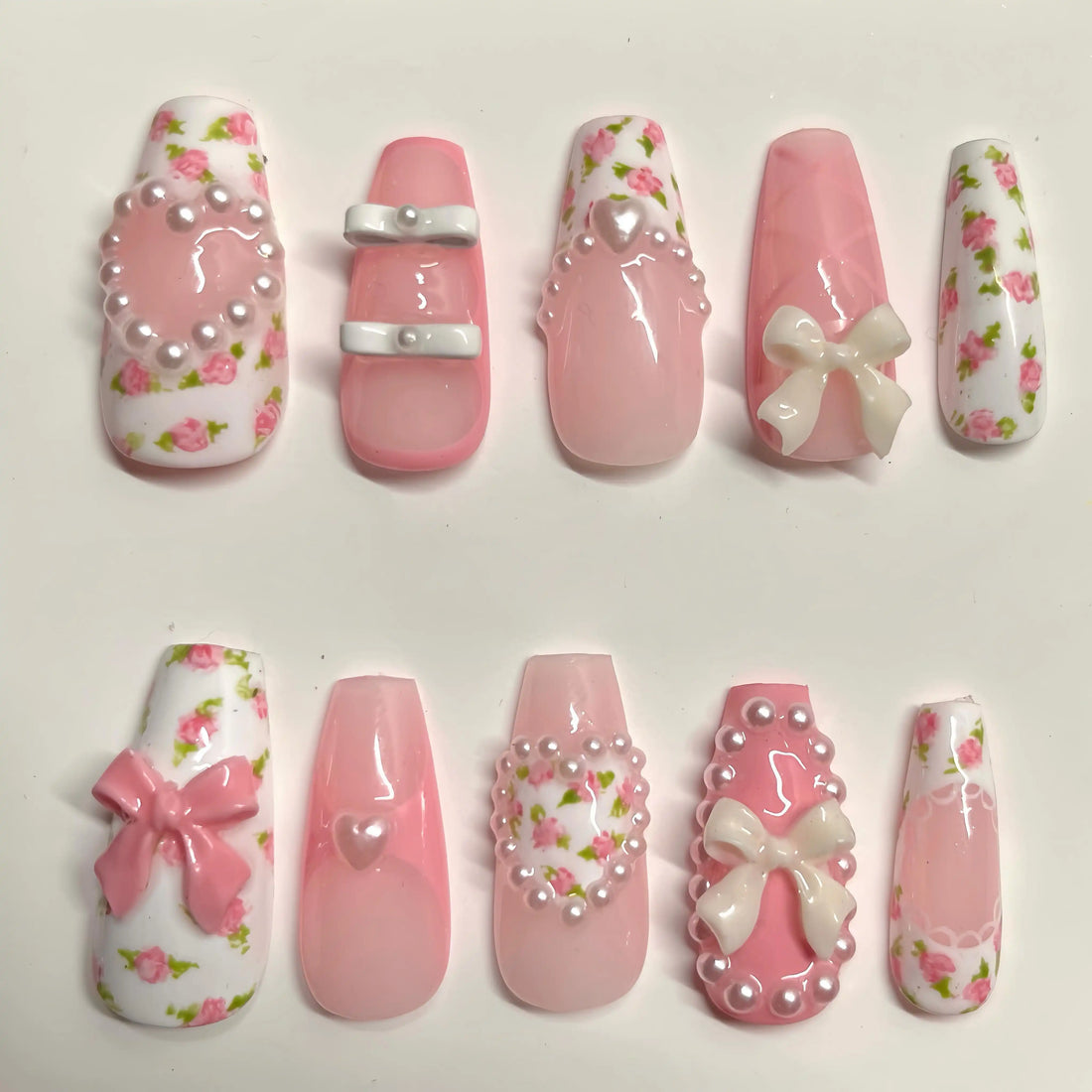 Handmade pink press-on nails with rose floral designs, 3D bows, pearls, and heart charms.
