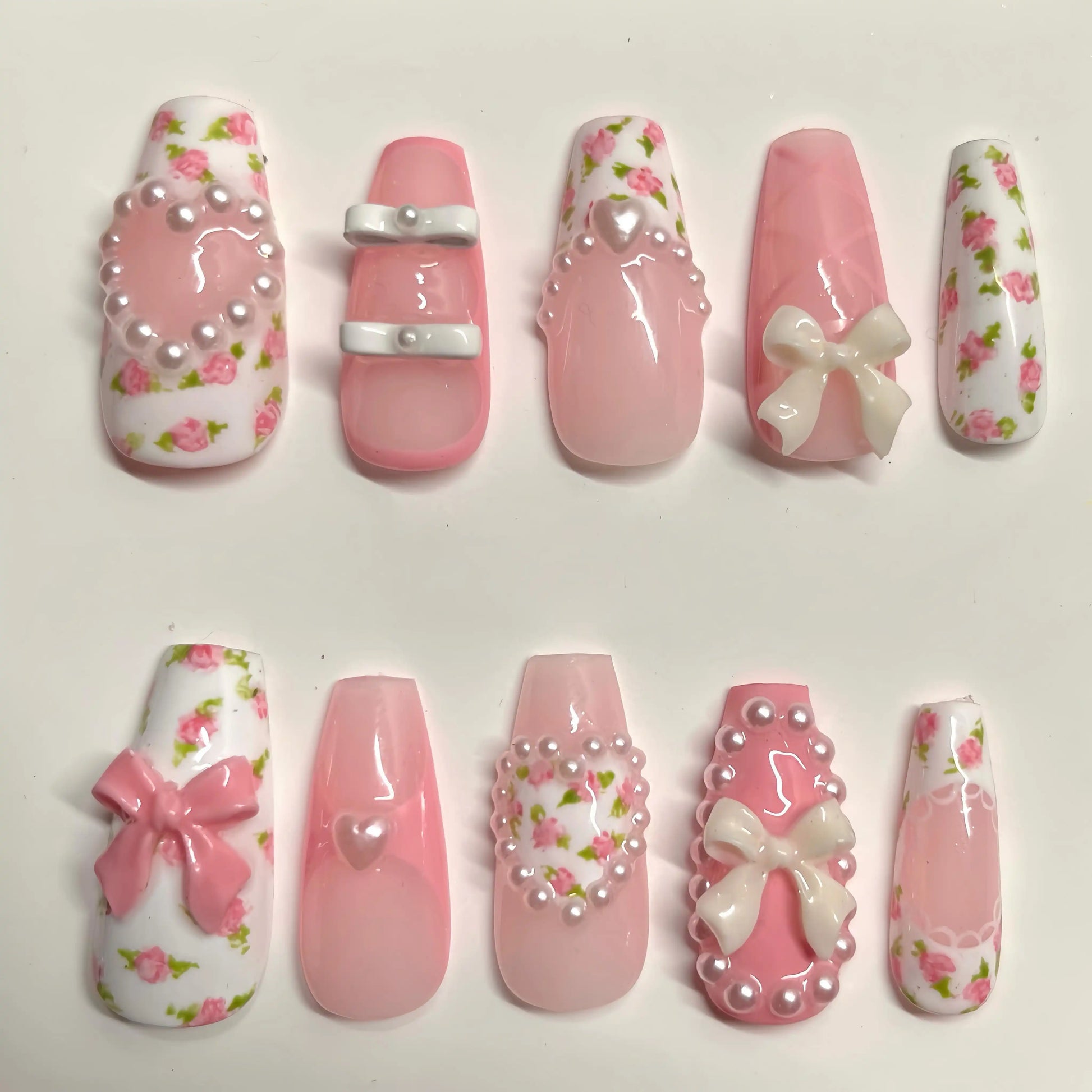 Handmade pink press-on nails with rose floral designs, 3D bows, pearls, and heart charms.