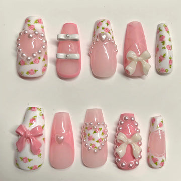 Handmade pink press-on nails with rose floral designs, 3D bows, pearls, and heart charms.