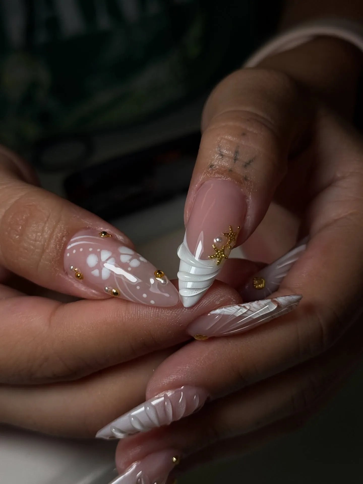 Hand holding white 3D shell floral press-on nails with gold stud accents, bridal nail art.
