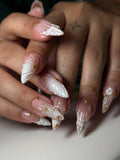 Hand with white 3D shell and floral press-on nails, gold studs, long pointed shape