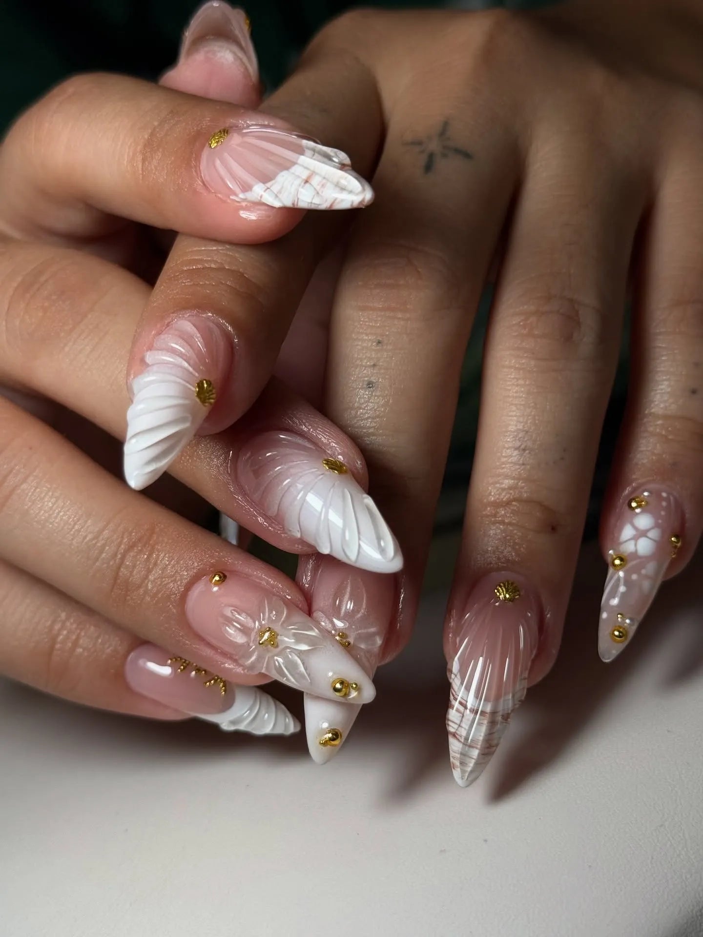 Hand with white 3D shell and floral press-on nails, gold studs, long pointed shape