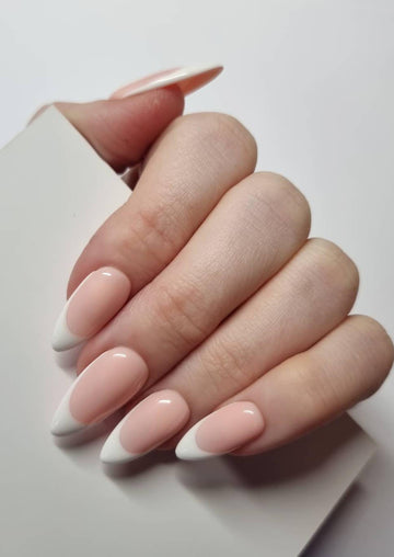 Hand displaying handmade white French tip press-on nails with almond shape