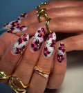 Hand with handmade white press-on nails featuring pink gothic floral art and gold dotted accents.