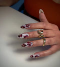 Hand with long white and pink floral press-on nails, gold dot accents, and gold rings