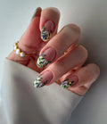 Hand with almond-shaped white French tip press-on nails featuring handmade wildflower meadow floral designs.