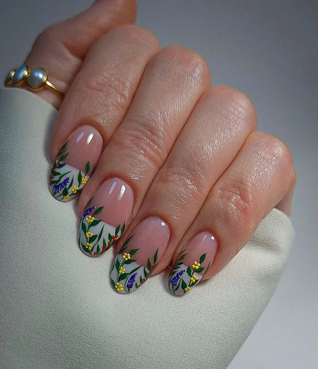 Hand with handmade white French tip press-on nails featuring wildflower meadow designs.